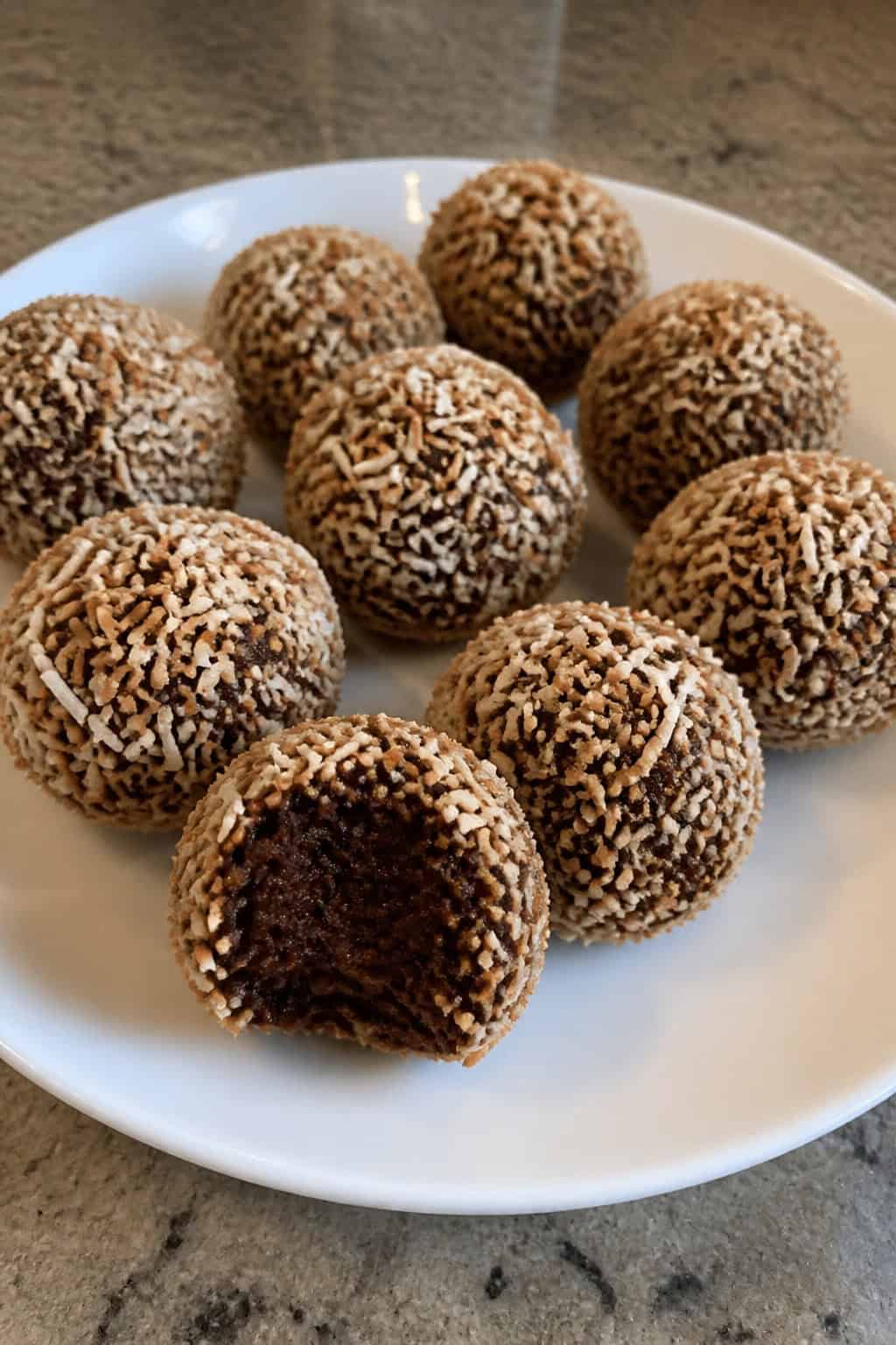 Close-up of chocolate brownie truffles rolled in toasted coconut arranged on a wooden board.
