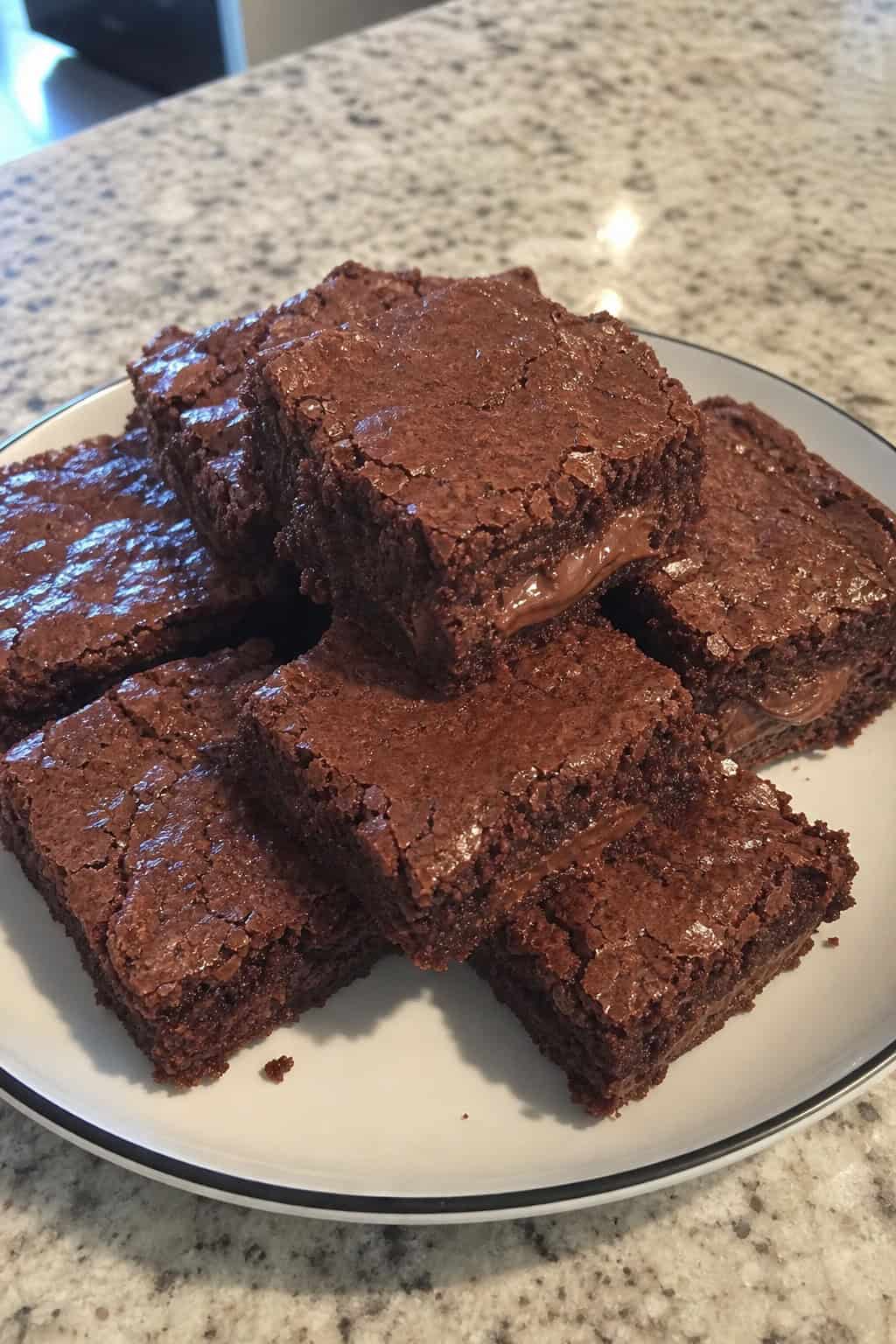 Close-up of brownies stuffed with Nutella, cut into squares and arranged on a wooden board with hazelnuts and a jar of Nutella nearby.