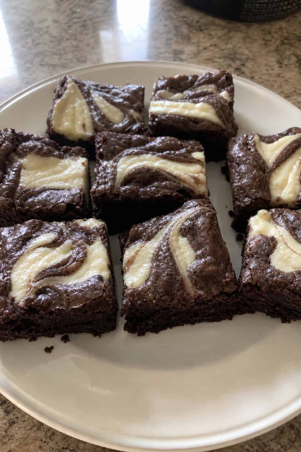 Close-up of brownie cheesecake swirl bars on a wooden board with baking ingredients in the background.