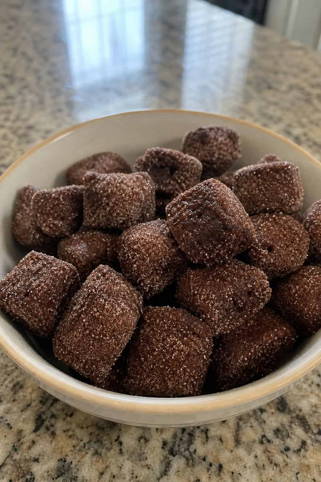 22 Recipes That Start With Brownie Mix 15 A bowl of cinnamon sugar coated brownie mix churro bites on a wooden surface with cinnamon sticks and sugar nearby.