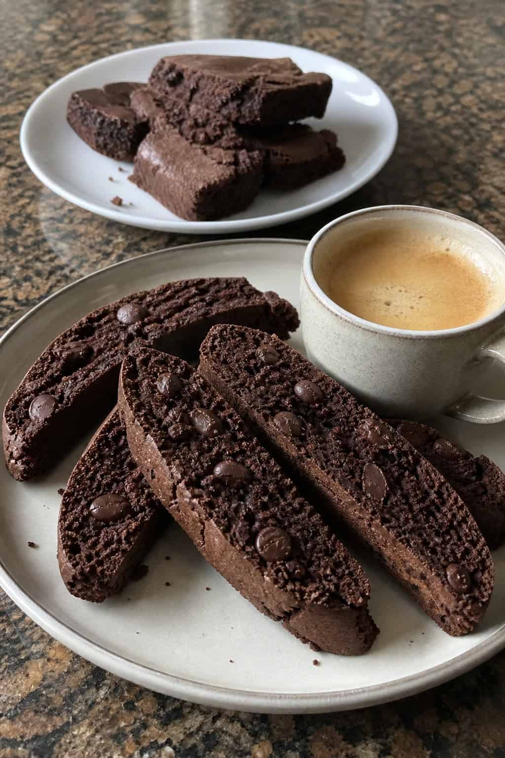 Close-up of espresso brownie biscotti on a wooden board next to a small cup of espresso and scattered coffee beans.