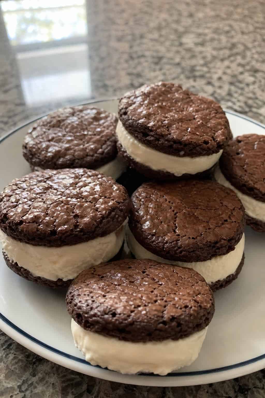 Close-up of brownie ice cream sandwich cookies on a wooden board with mint leaves and chocolate chunks nearby.