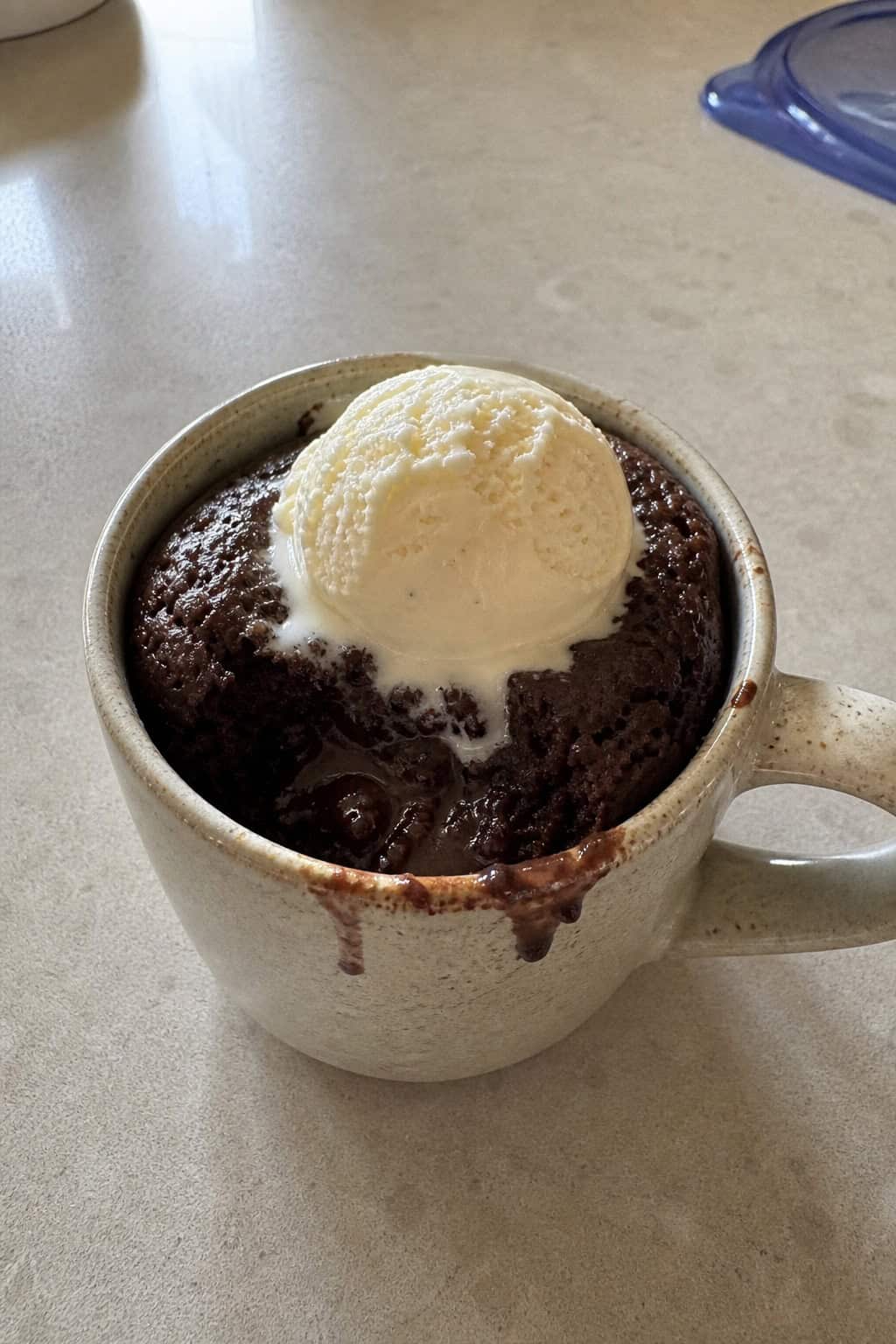 A mug filled with molten brownie topped with melting vanilla bean ice cream on a wooden table.