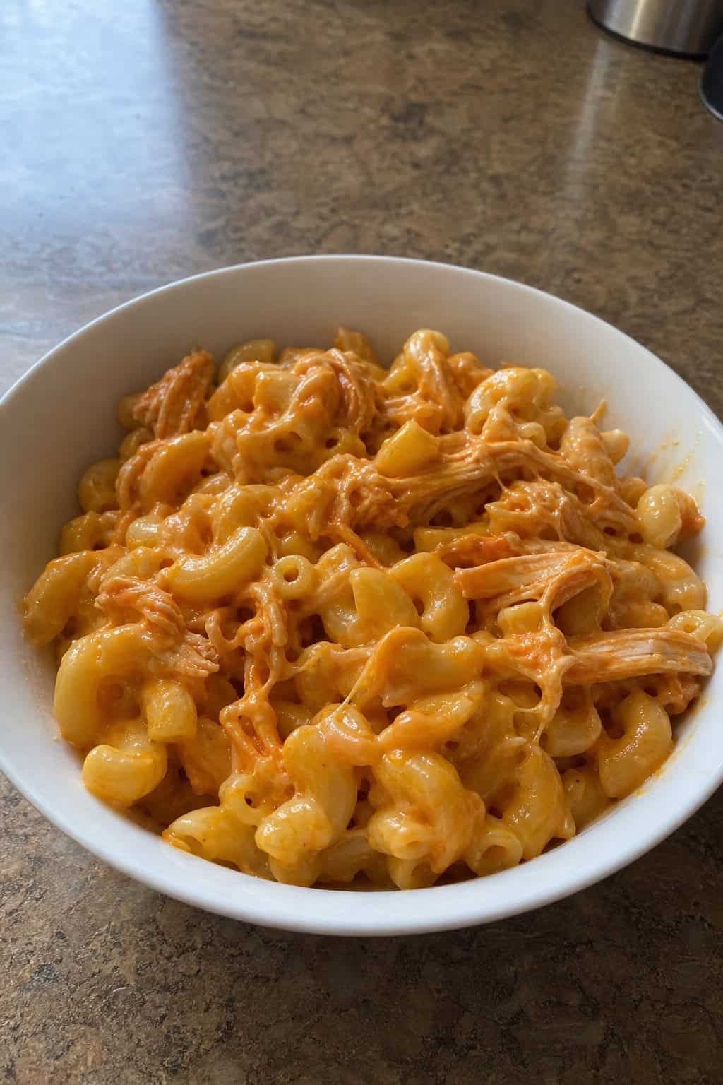 A bowl of buffalo chicken mac and cheese garnished with green onions on a wooden table.