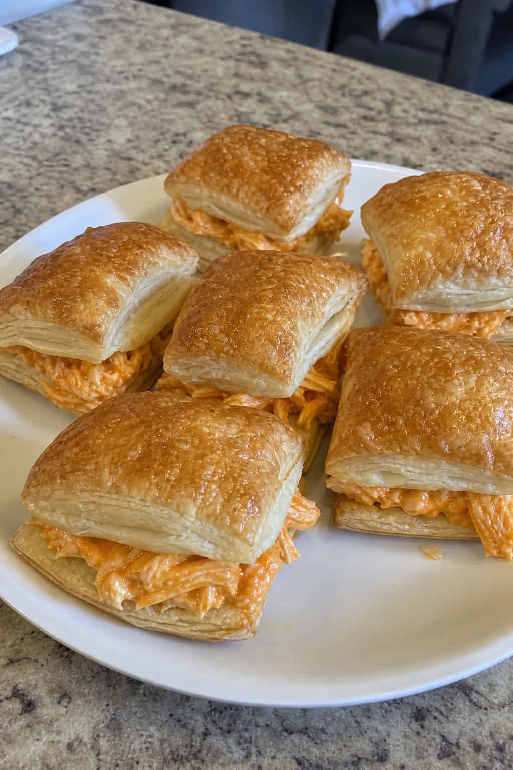 Close-up of buffalo chicken puff pastry sliders on a wooden board with a small bowl of dipping sauce and celery sticks in the background.
