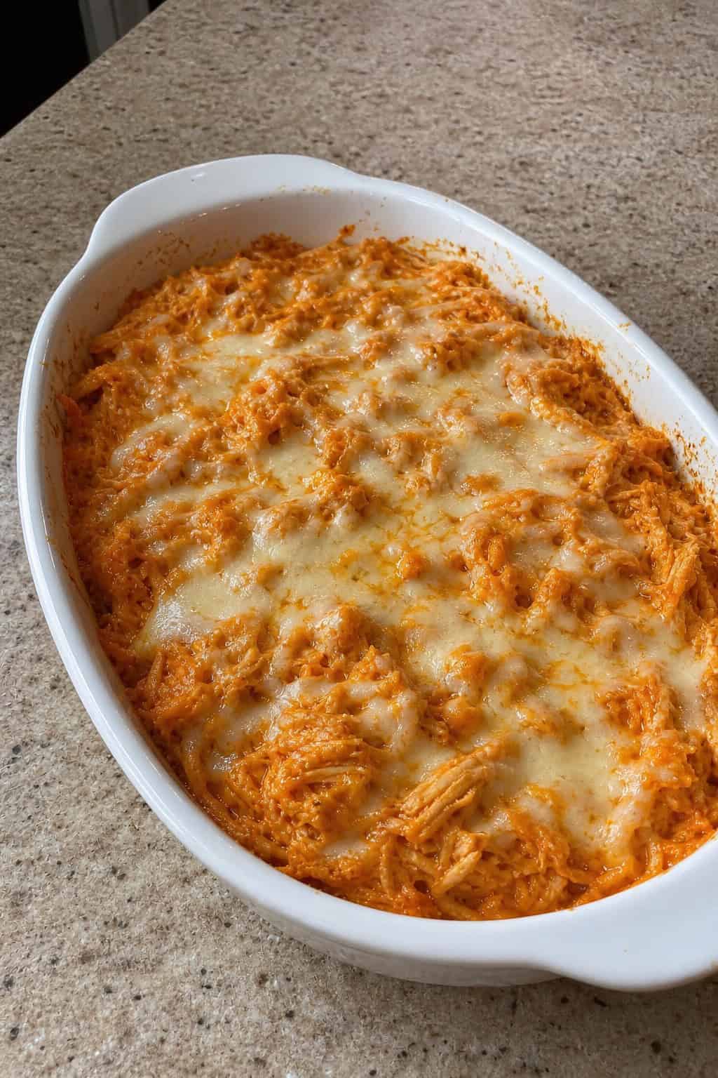 22 Chicken and Spaghetti Squash Recipes You’ll Love to Try Tonight! 6 A baked dish of buffalo chicken spaghetti squash topped with melted cheese and green onions on a wooden table with a bowl of ranch dressing and celery sticks nearby.