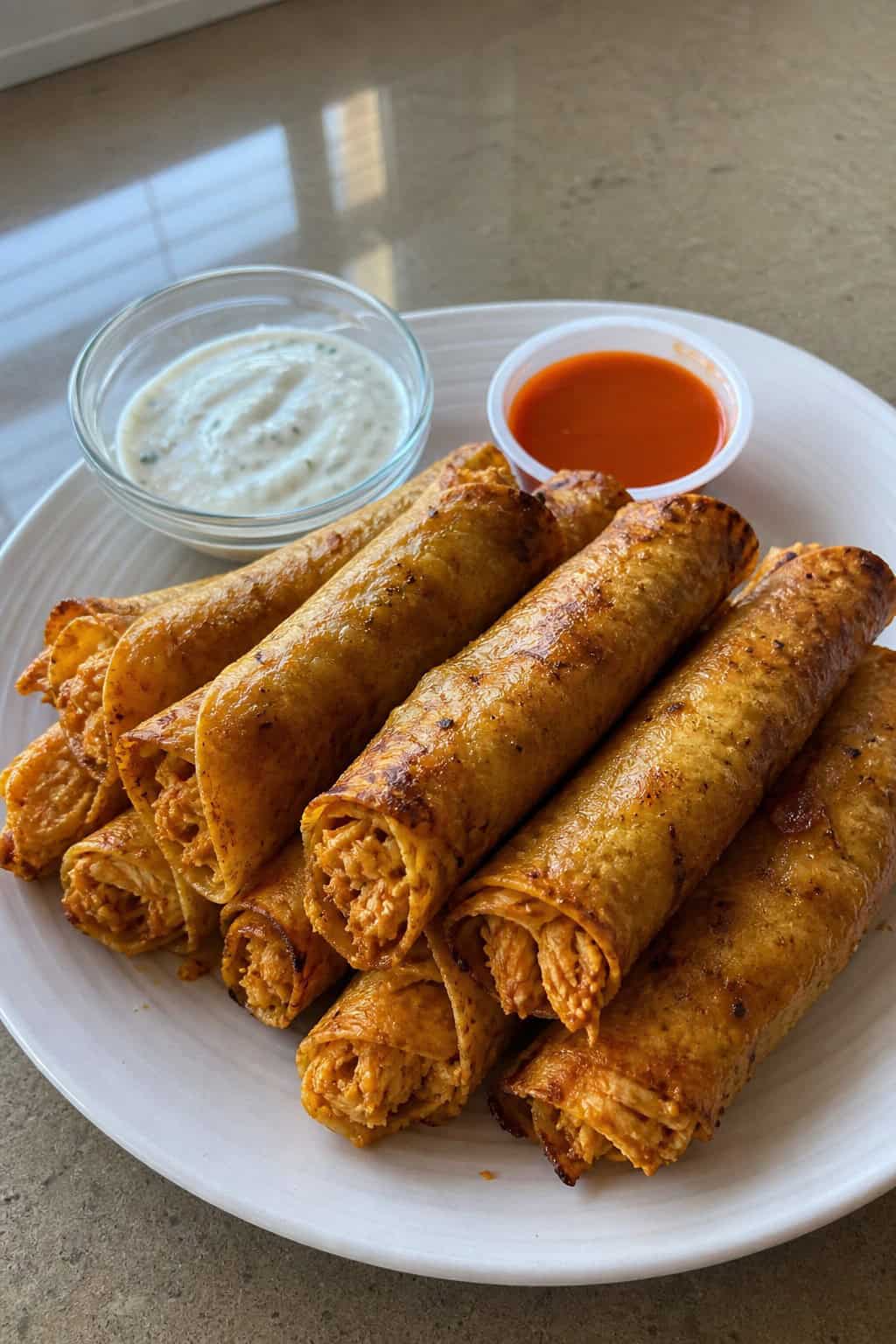 A platter of crispy buffalo chicken taquitos with dipping sauces and garnishes on a wooden table.