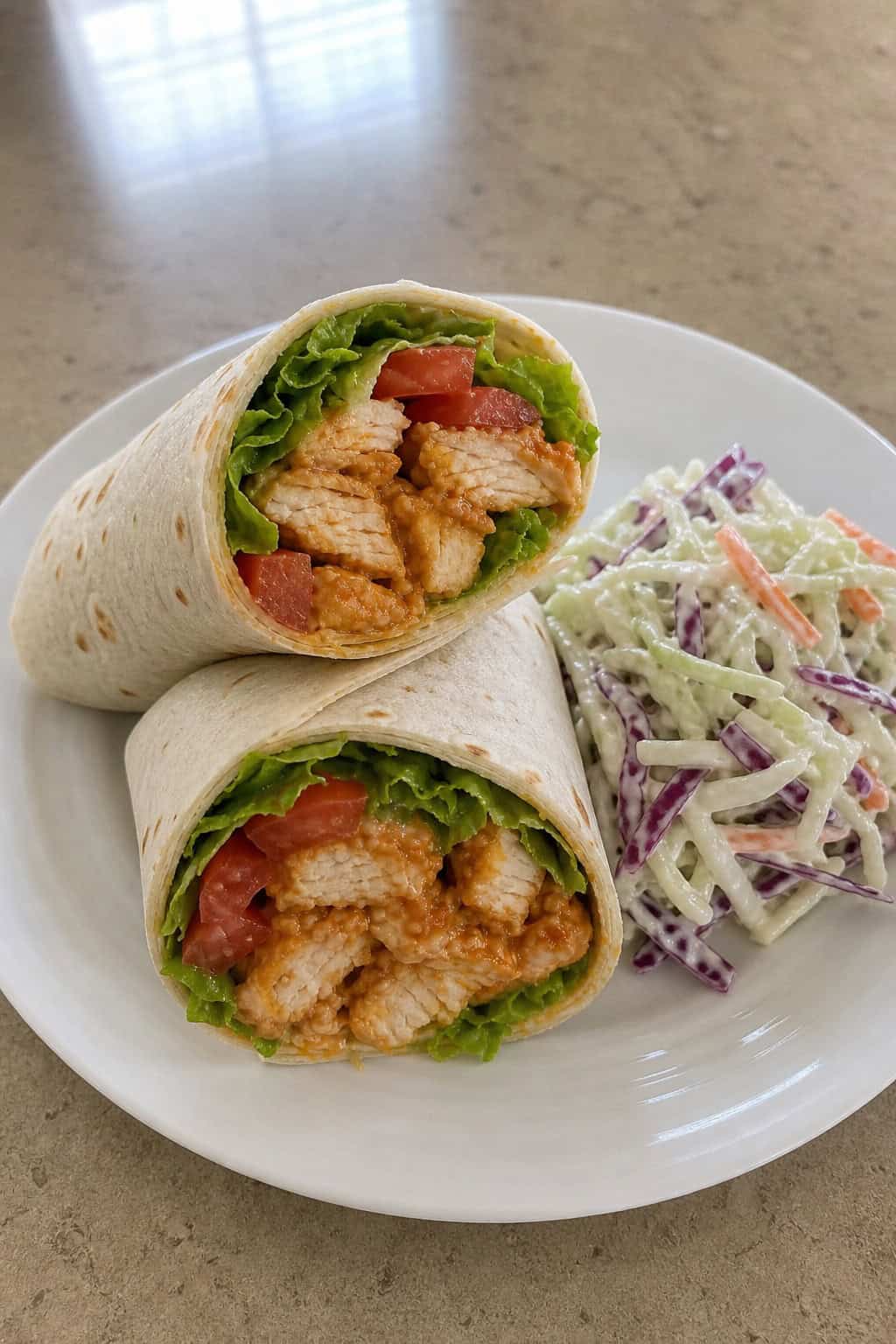 Plate of buffalo chicken wraps with blue cheese slaw and celery sticks on a wooden table.
