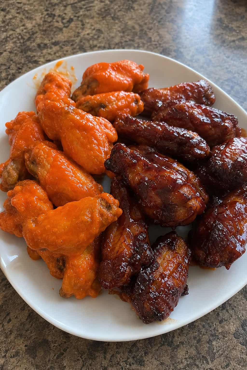 A plate of Buffalo and honey BBQ chicken wings with ranch dipping sauce and celery sticks on a wooden platter.
