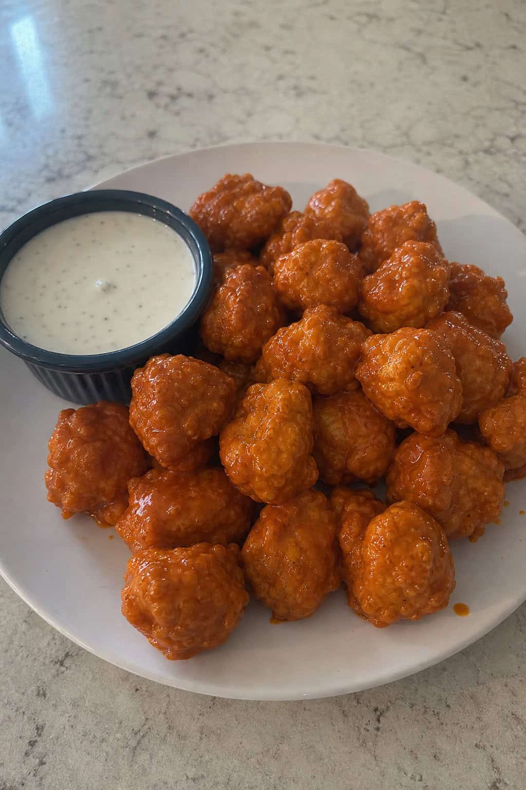 Plate of buffalo-style chicken bites with a bowl of ranch dip on a wooden table.