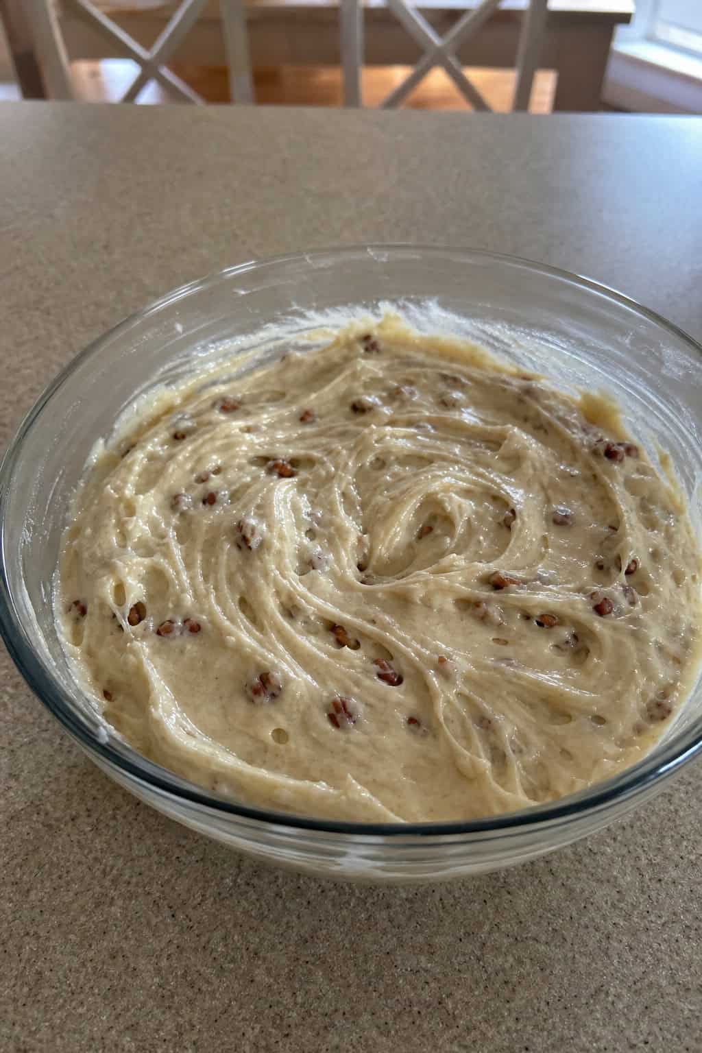 A bowl of creamy butter pecan rum cheesecake filling with pecans and rum bottle on a wooden surface.