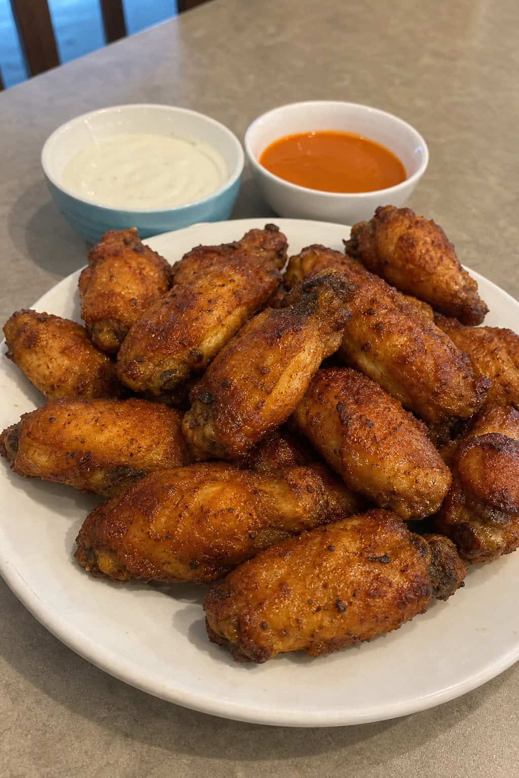 A plate of crispy chicken wings seasoned with paprika, garnished with parsley, and served with dipping sauces on a wooden table.