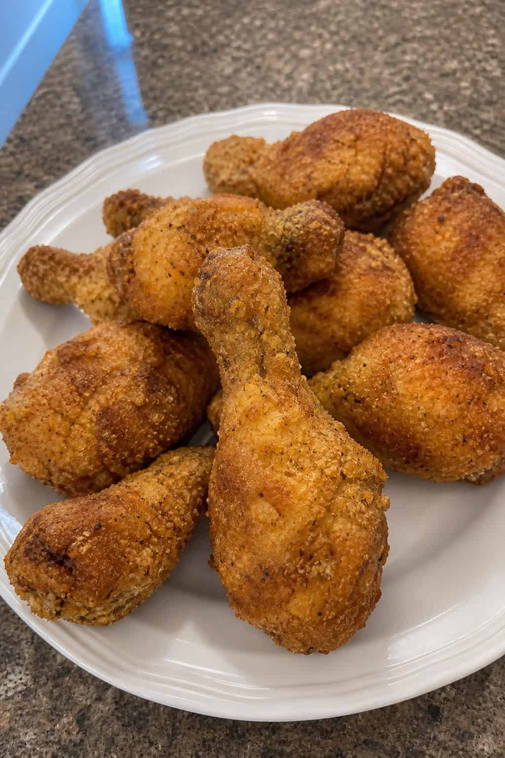 Golden panko-crusted chicken drumsticks stacked on a white plate with a small bowl of creamy ranch dipping sauce and a scattering of fresh herb leaves on a wood surface.