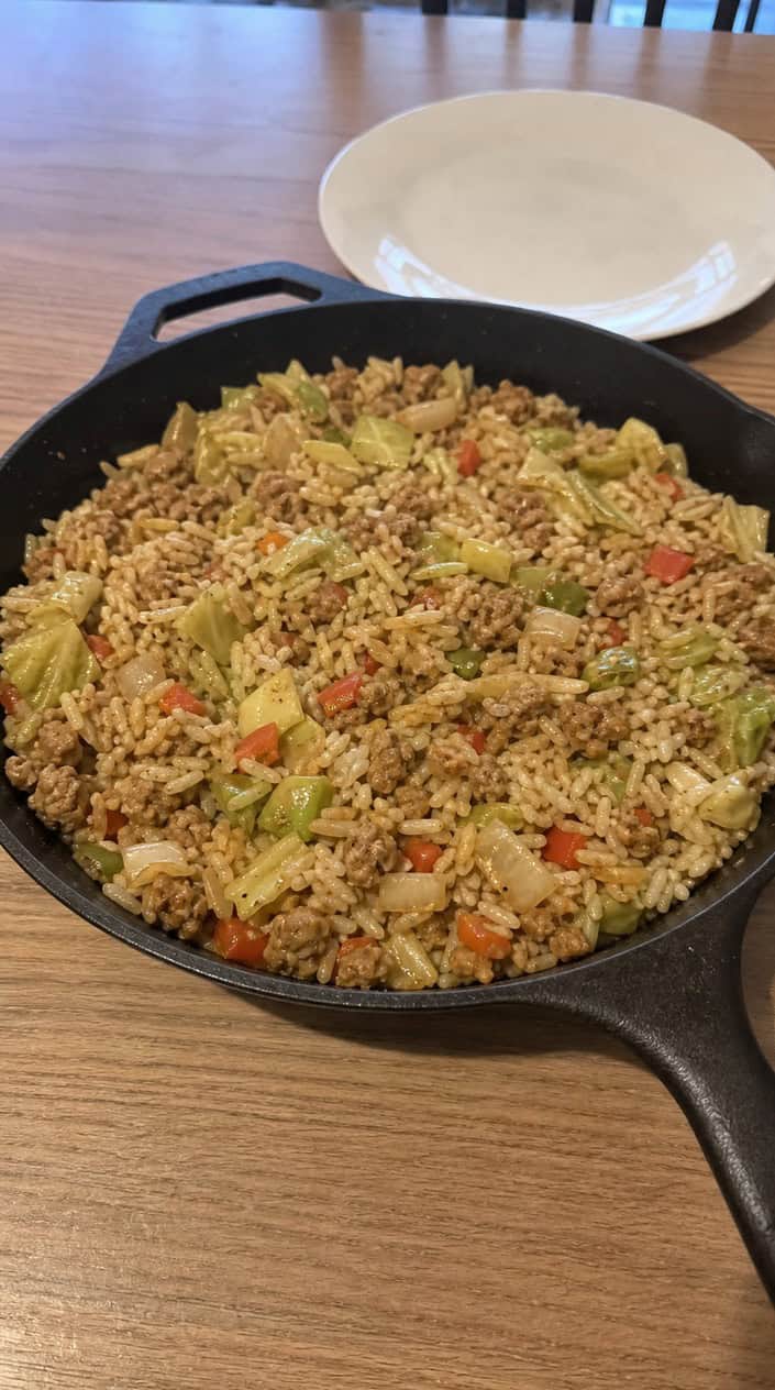Skillet filled with ground chicken, rice, and pieces of cabbage on a wooden table.