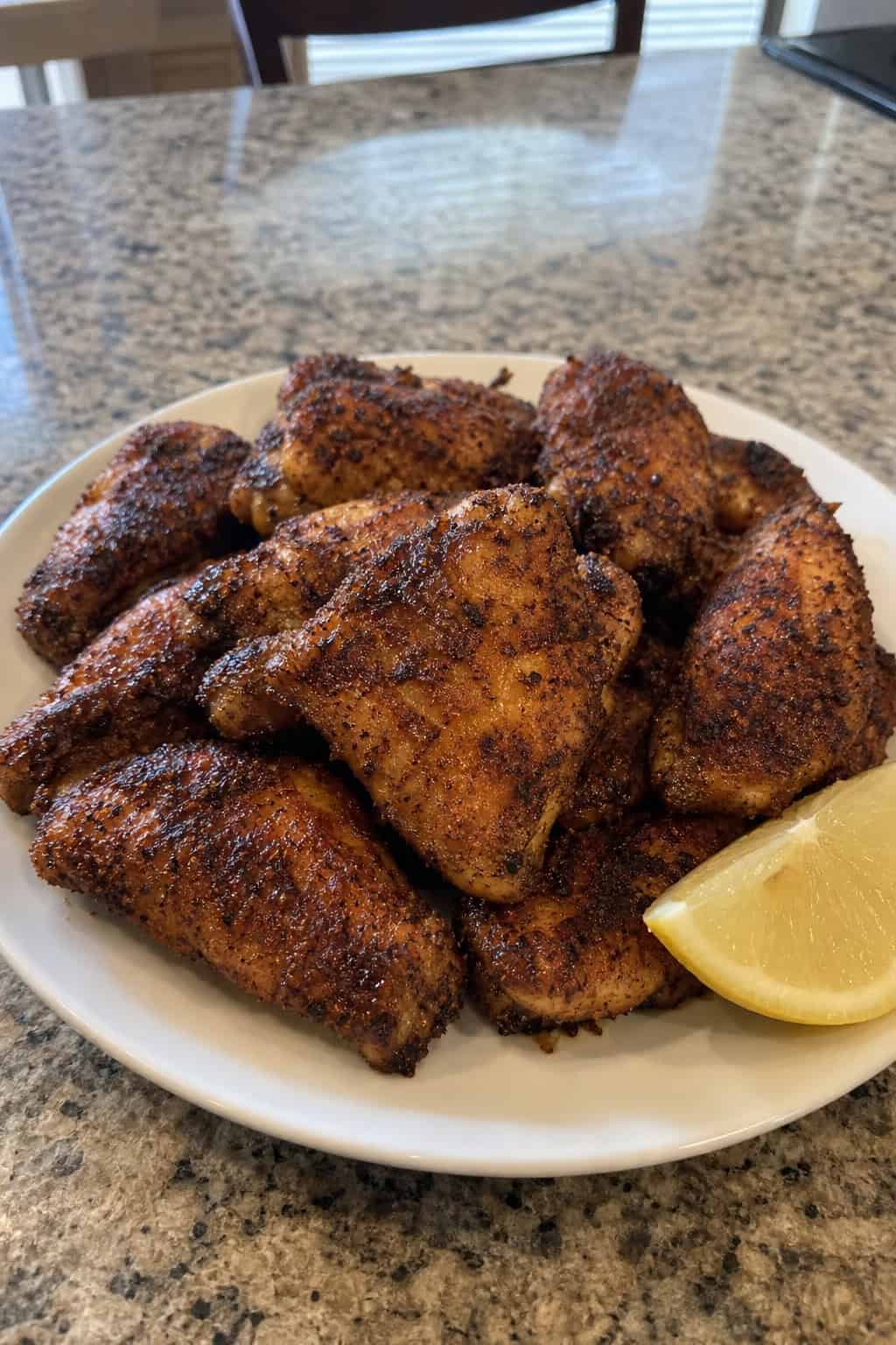 A plate of crispy Cajun blackened chicken wings with a lemon wedge on a wooden table.