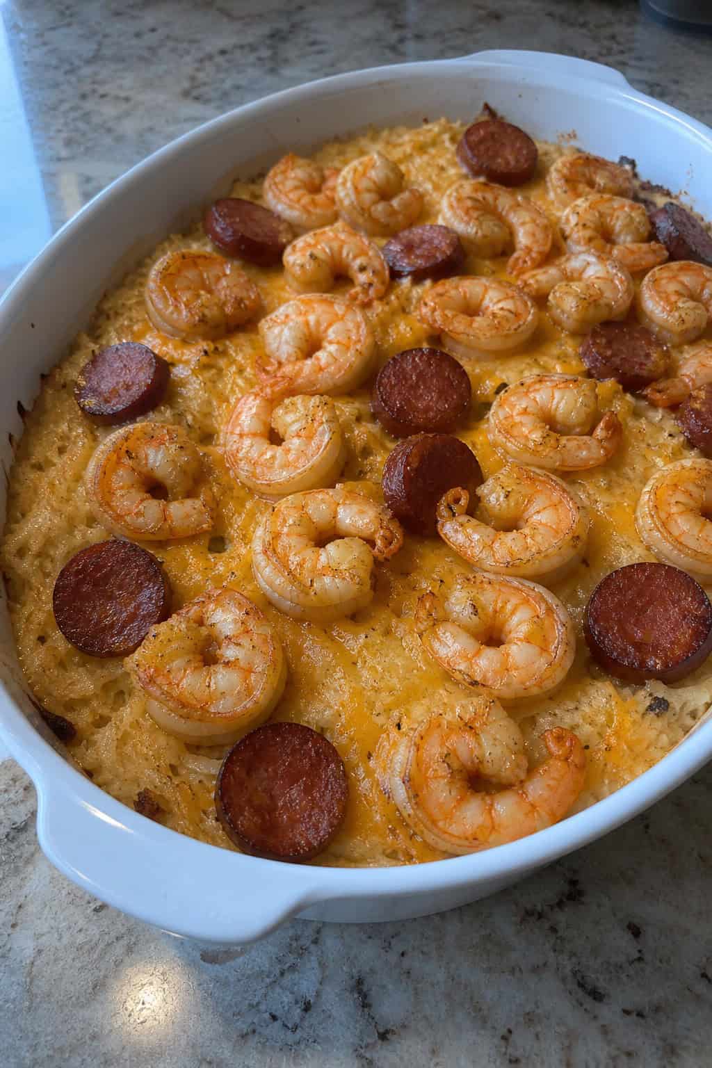 A baked casserole dish filled with shrimp, sausage, and crispy hashbrowns garnished with parsley on a wooden table.