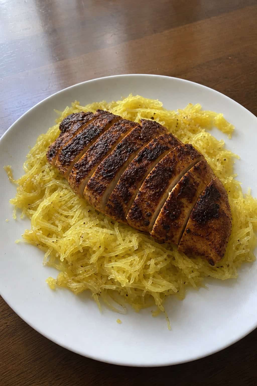 A plate of Cajun-spiced chicken served over garlic butter spaghetti squash garnished with fresh herbs on a wooden table.