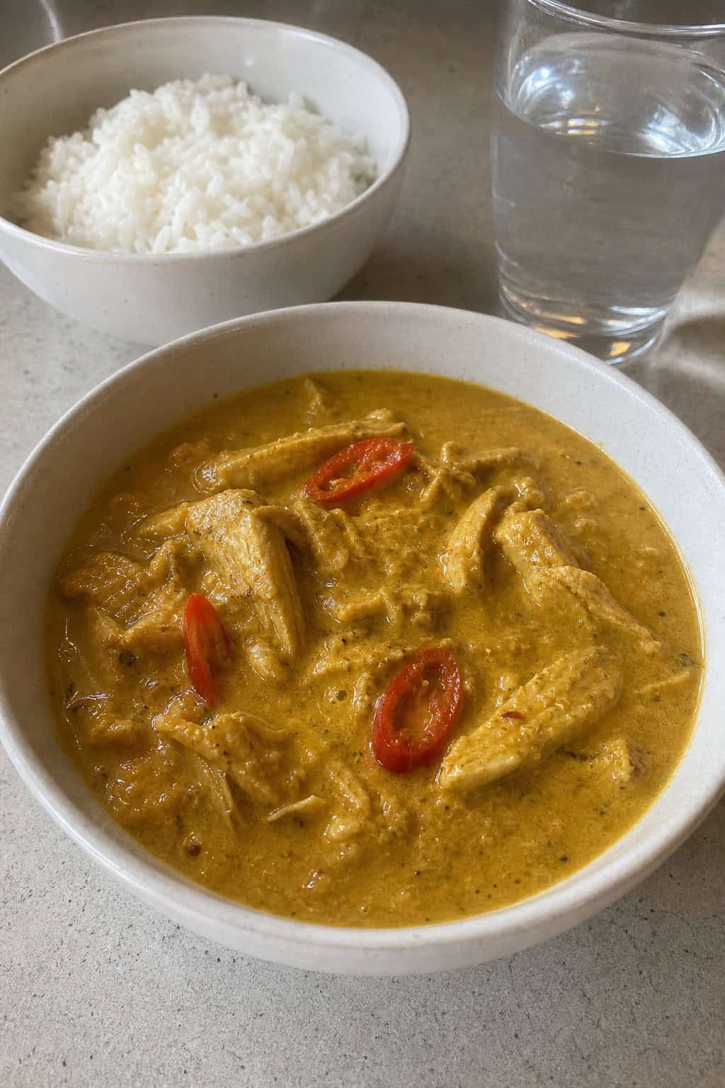 A bowl of creamy canned chicken curry with coconut milk garnished with cilantro and red chili, served on a wooden table with a bowl of rice in the background.