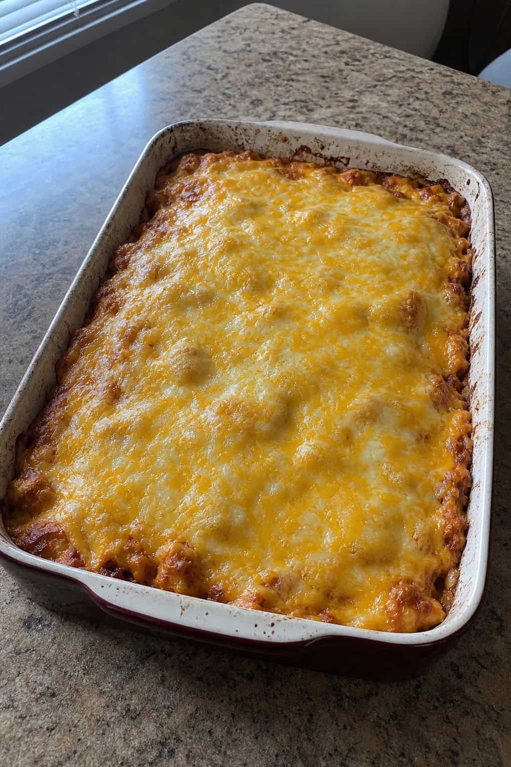 A baked chicken enchilada casserole in a ceramic dish garnished with cilantro and green onions on a kitchen countertop with cooking ingredients around it.