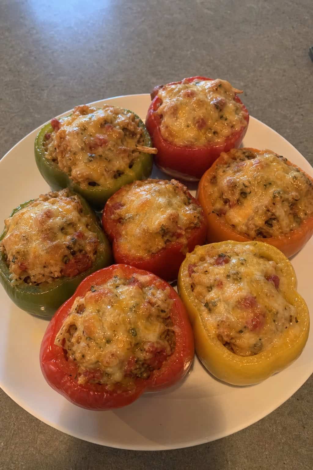 A plate of colorful bell peppers stuffed with a chicken and vegetable filling, garnished with herbs, surrounded by fresh ingredients on a wooden surface.