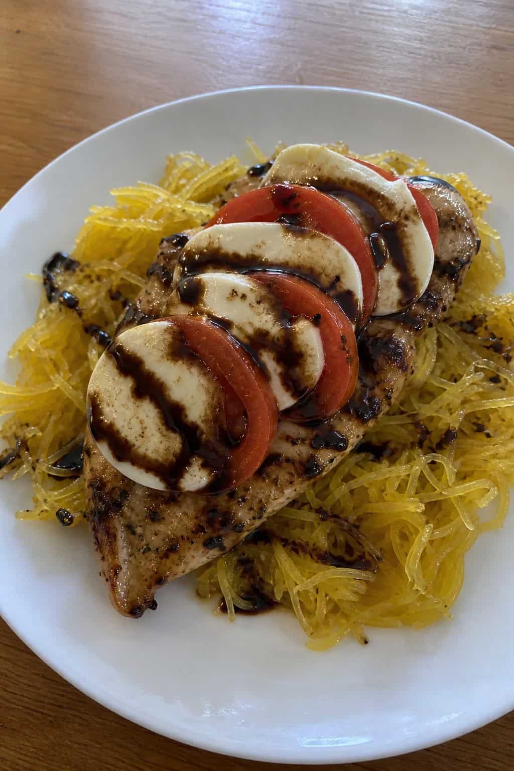 A plate of Caprese chicken on roasted spaghetti squash, topped with tomato slices, mozzarella, basil, and balsamic drizzle.