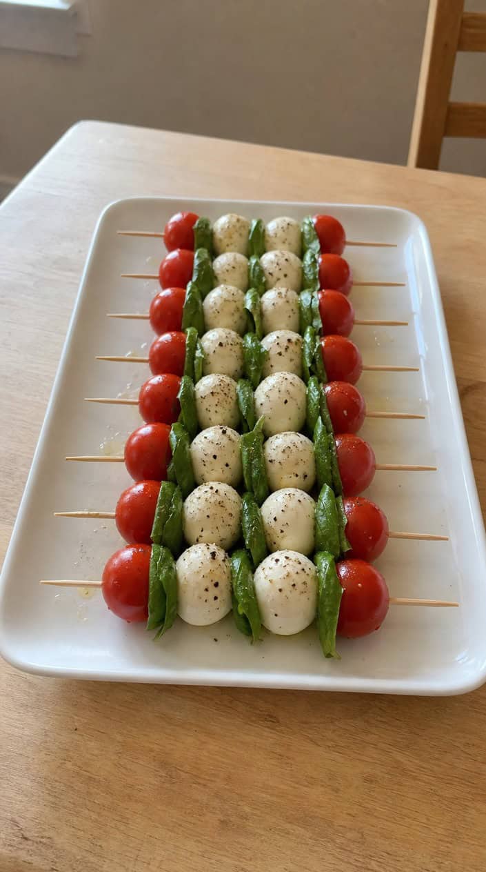 A plate of Caprese skewers with cherry tomatoes, basil leaves, and mozzarella balls arranged neatly.