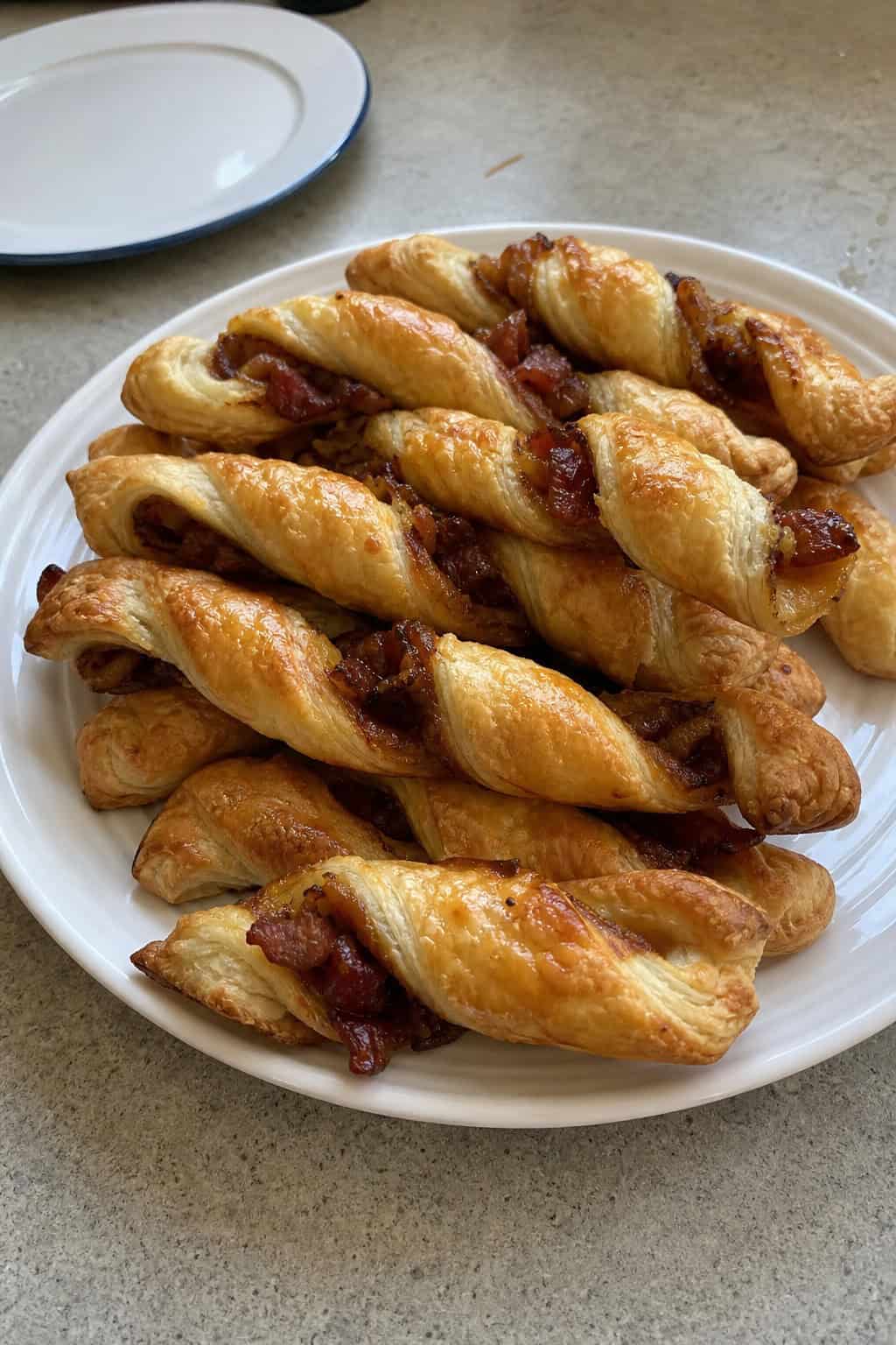 Close-up of golden brown puff pastry twists with bacon and caramelized onions on a wooden board with fresh herbs.