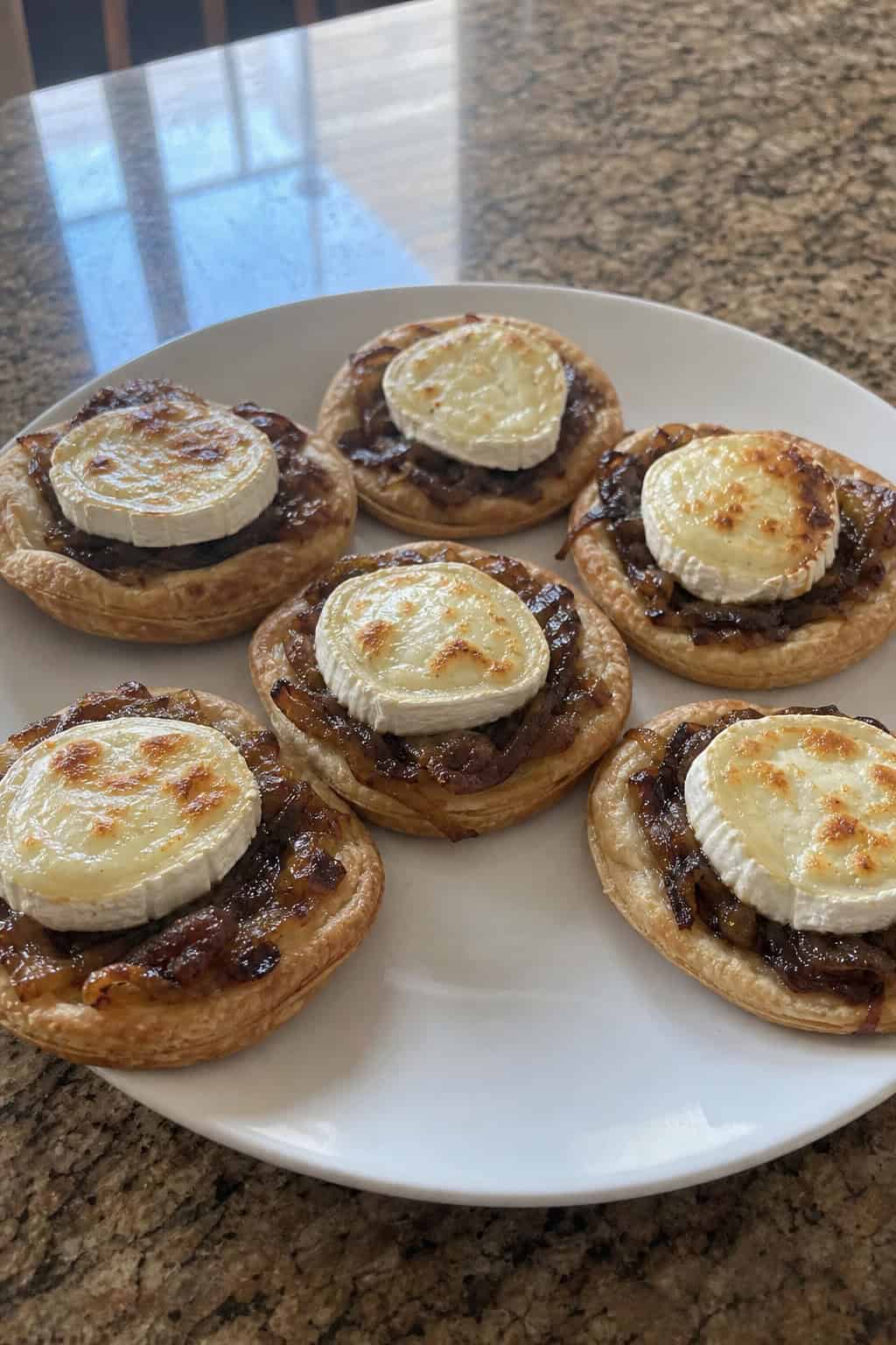 Several caramelized-onion and goat cheese tarts arranged on a wooden board with fresh herbs.