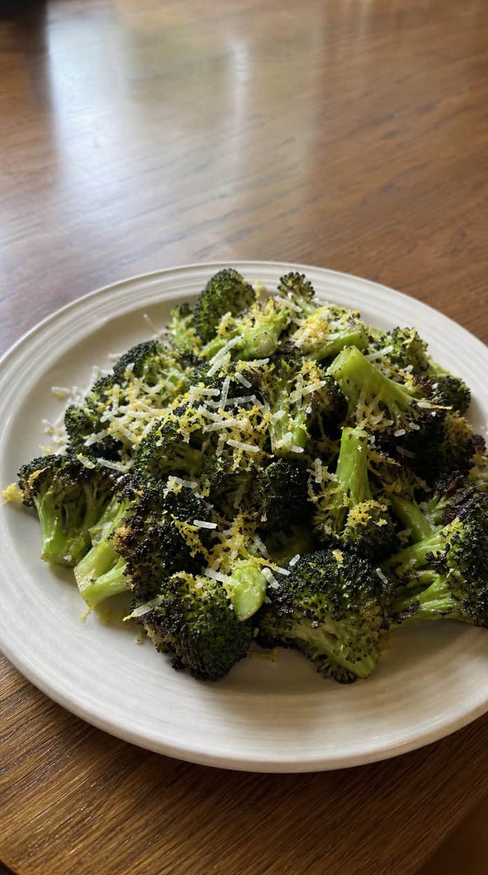 A plate of grilled broccoli topped with lemon zest and grated Parmesan cheese on a wooden table.