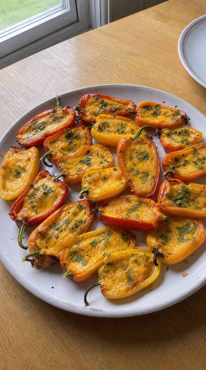 A plate of colorful mini bell peppers stuffed with melted cheddar cheese, garnished with fresh herbs.