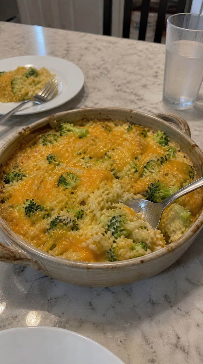 A freshly baked cheesy broccoli rice casserole in a ceramic dish on a wooden table with a serving spoon.