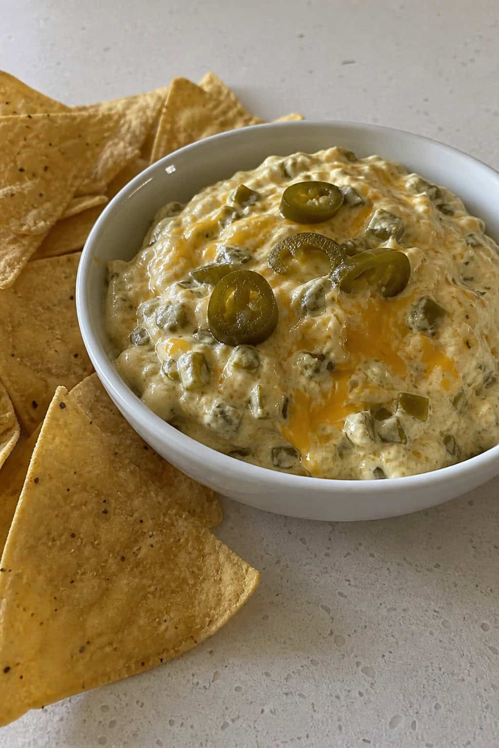 A bowl of creamy cheesy jalapeño popper dip with chopped jalapeños and tortilla chips on a wooden table.