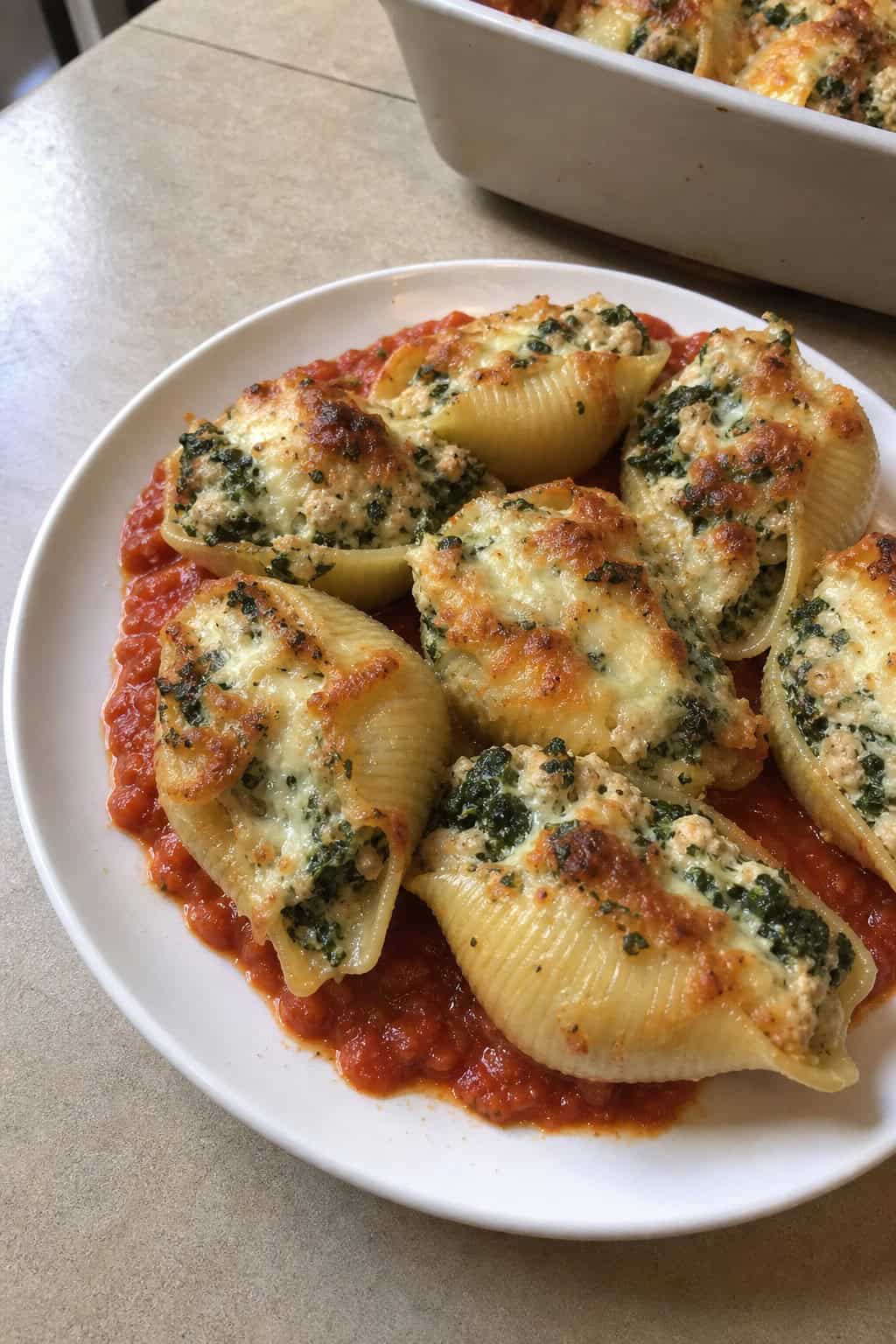 A plate of cheesy minced chicken and spinach stuffed pasta shells garnished with parsley and tomato sauce on a wooden table.
