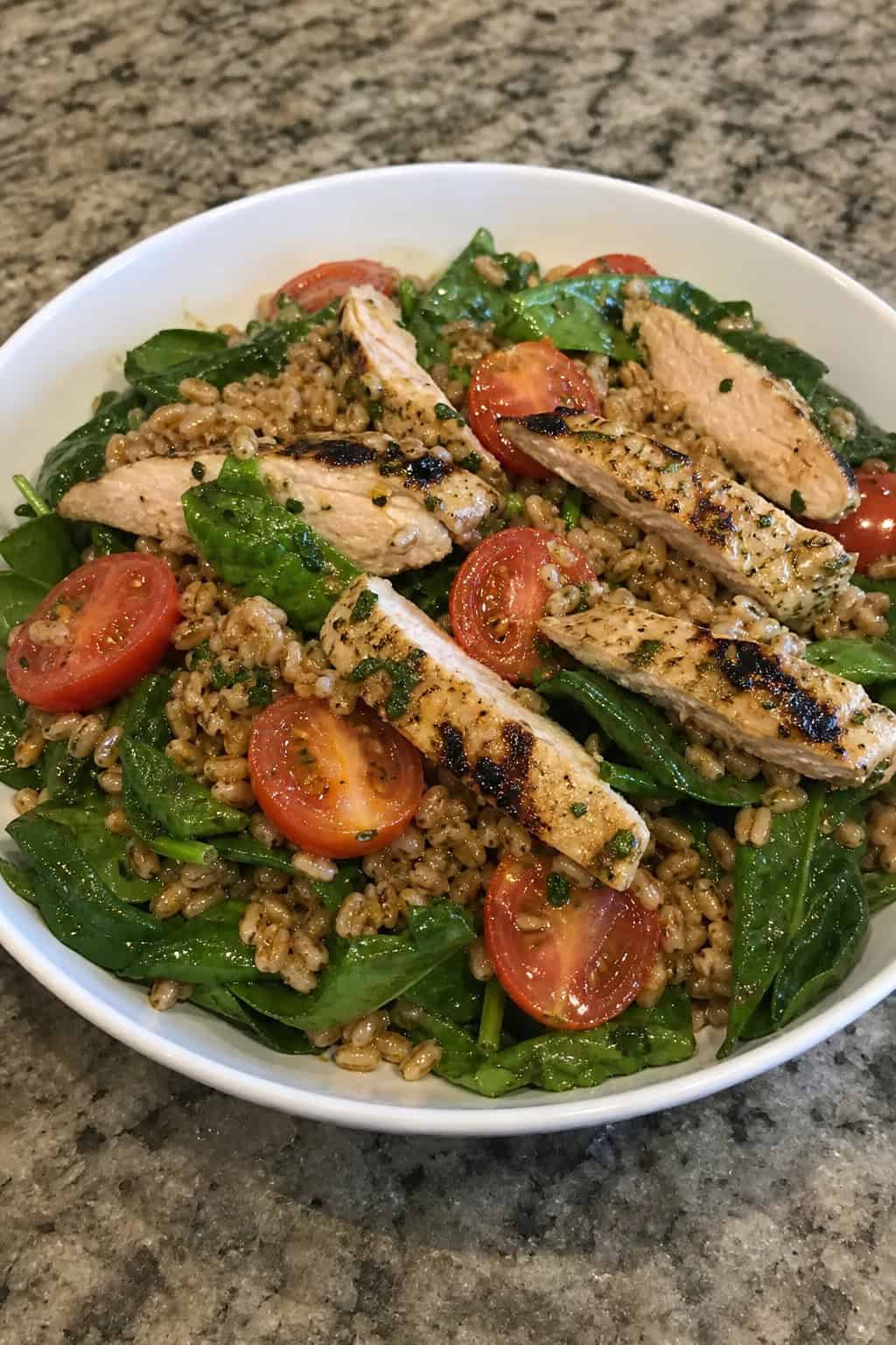 25 Heart-Healthy Chicken Recipes to Keep You Feeling Great! 17 A bowl of chicken and farro salad with cherry tomatoes and greens on a wooden table.