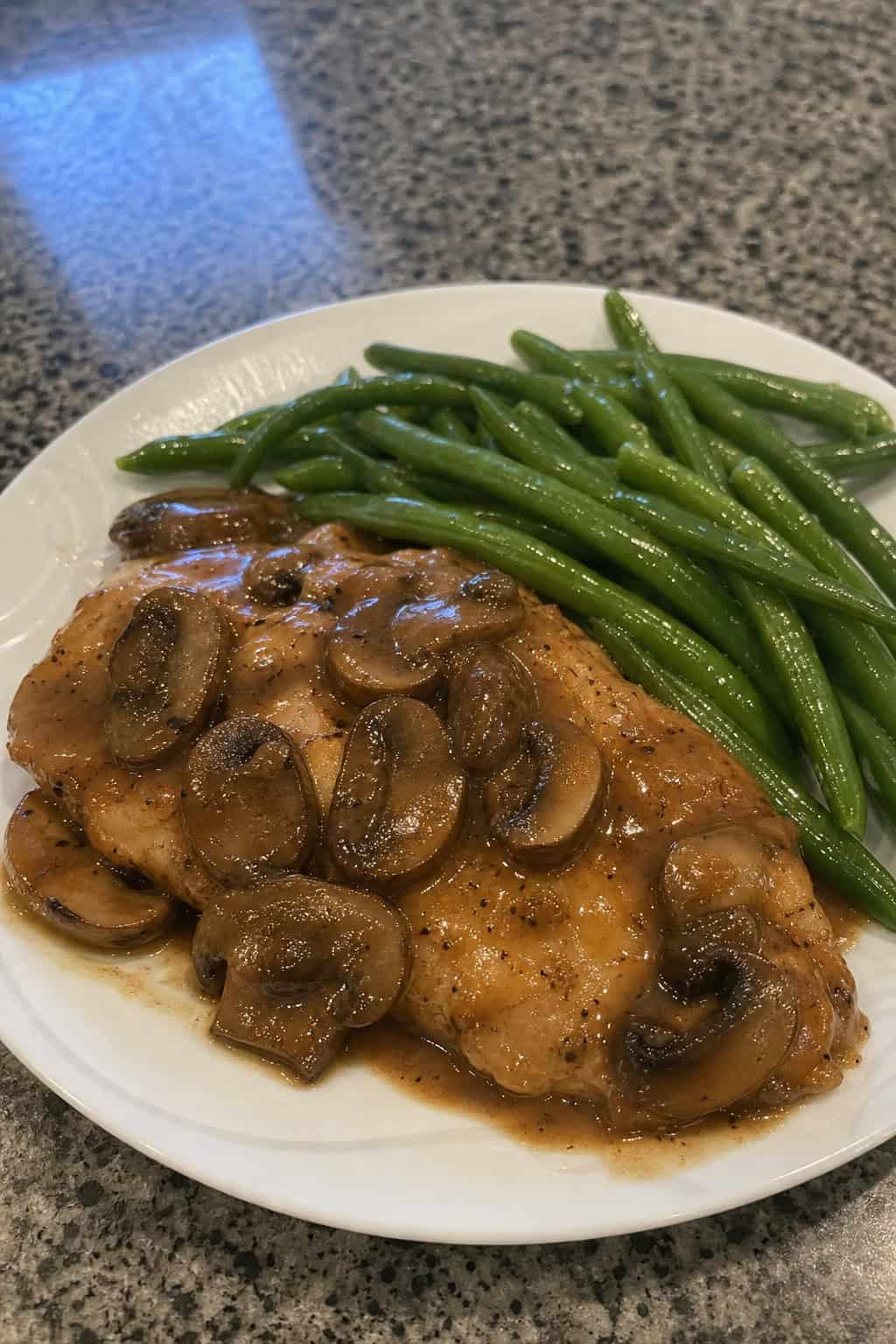 Plate of chicken with mushroom sauce served with steamed green beans on a table.