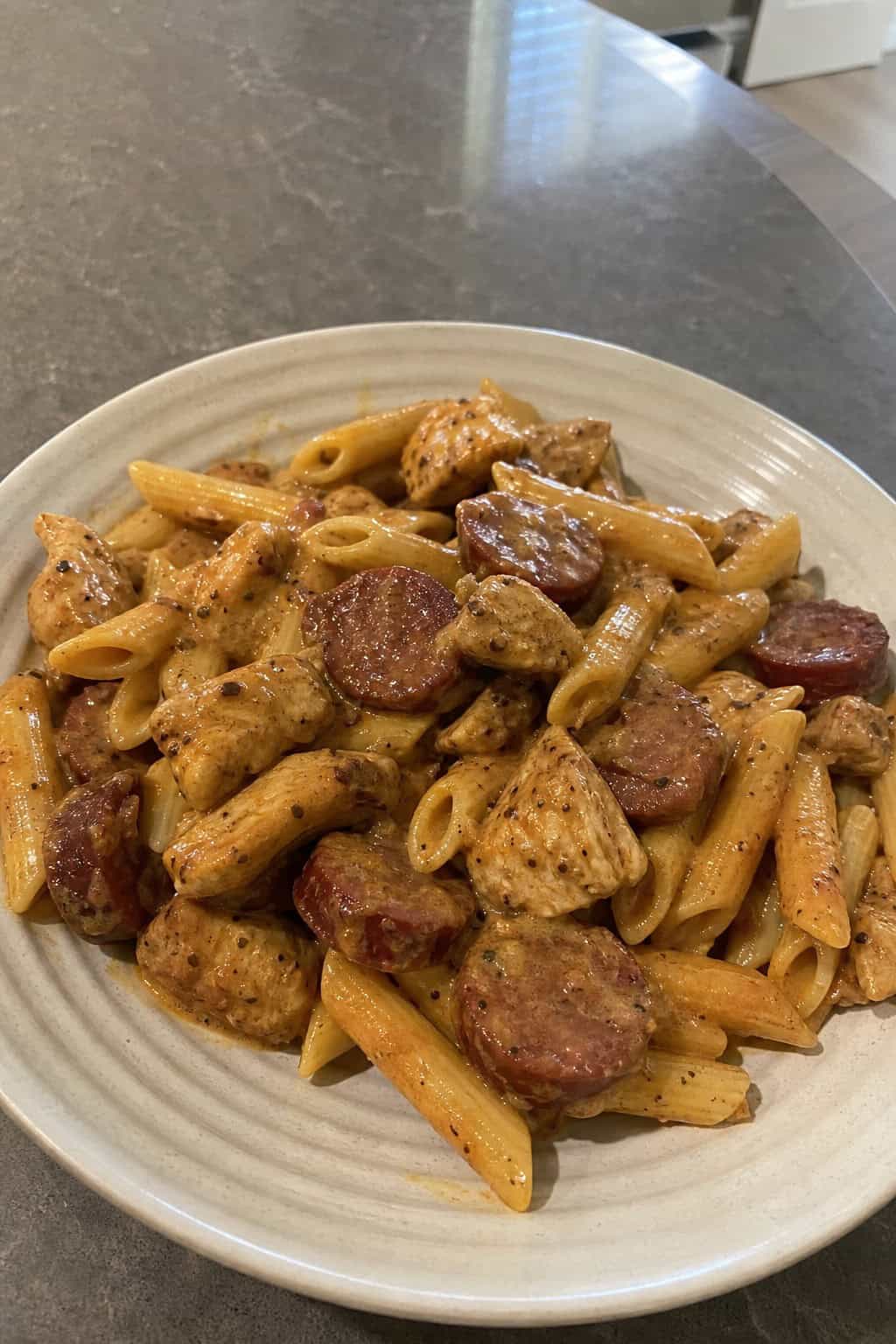 A bowl of chicken and sausage Cajun pasta garnished with parsley on a wooden table with ingredients in the background.
