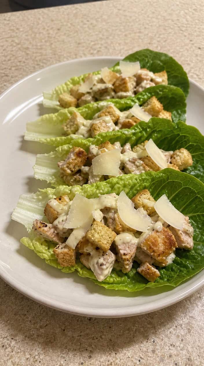Chicken Caesar lettuce wraps on a wooden board with lemon wedges and a bowl of dressing on a light table.