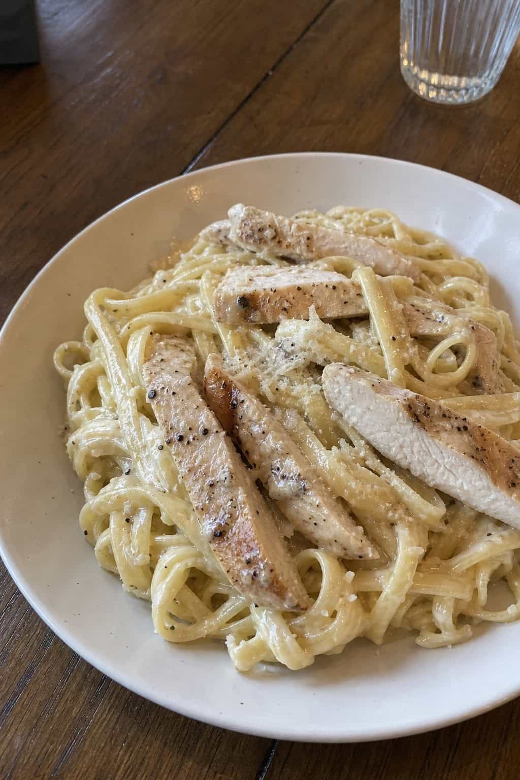 A bowl of creamy chicken carbonara pasta made with turkey, garnished with parsley and Parmesan cheese on a wooden table.