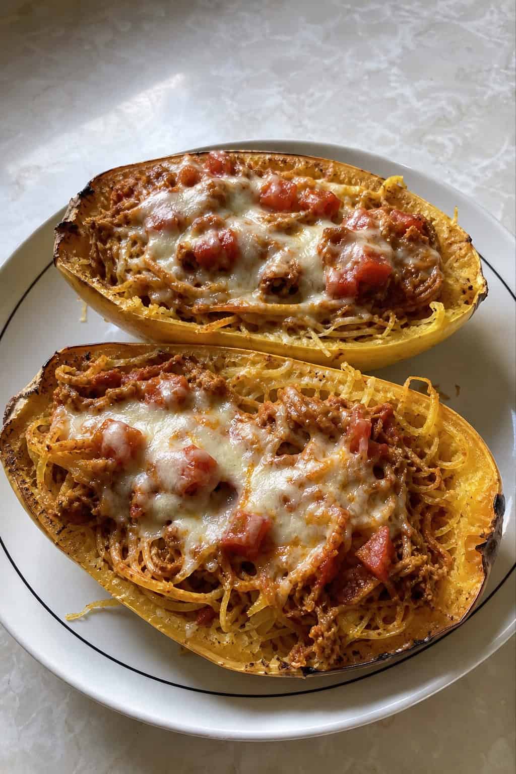 Two spaghetti squash halves filled with chicken enchilada mixture, garnished with cheese and cilantro, on a wooden table with bowls of fresh ingredients around them.