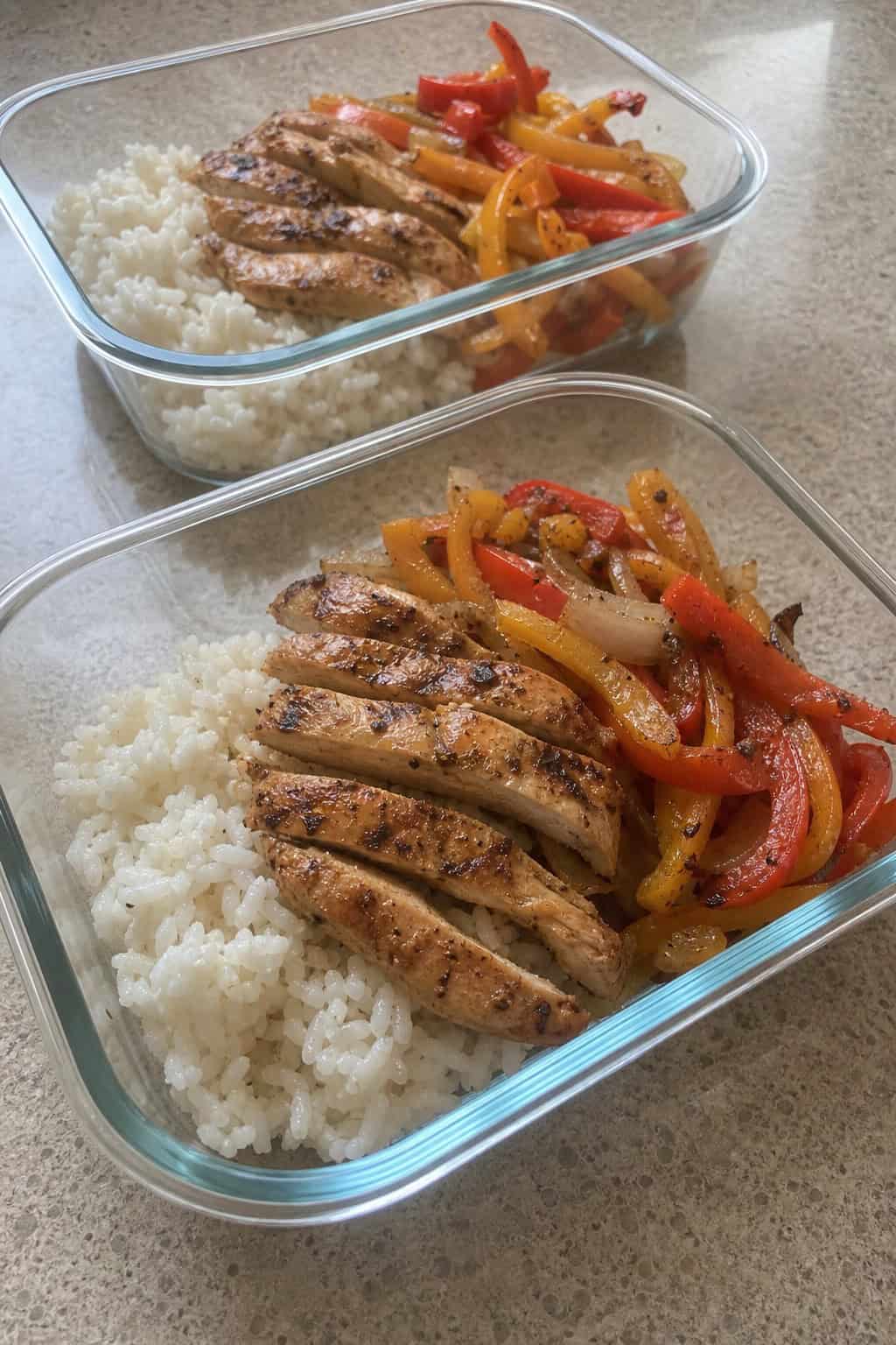 Meal-prep bowls filled with grilled chicken strips, sautéed bell peppers, onions, rice, and garnished with cilantro and lime wedges.