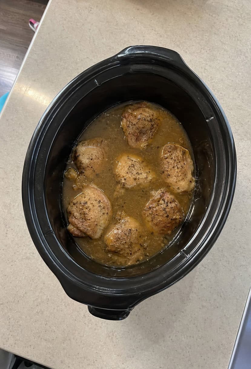 A crockpot filled with Chicken Marsala surrounded by ingredients and a recipe book