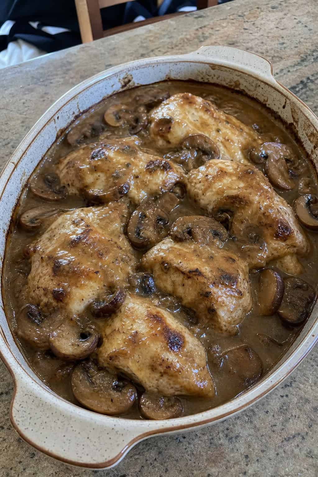 20 Chicken Casserole Recipes for Big Gatherings 21 A baked chicken and cremini mushroom casserole in a deep ceramic dish with a golden mozzarella and Parmesan topping, garnished with fresh flat-leaf parsley on a wooden table.