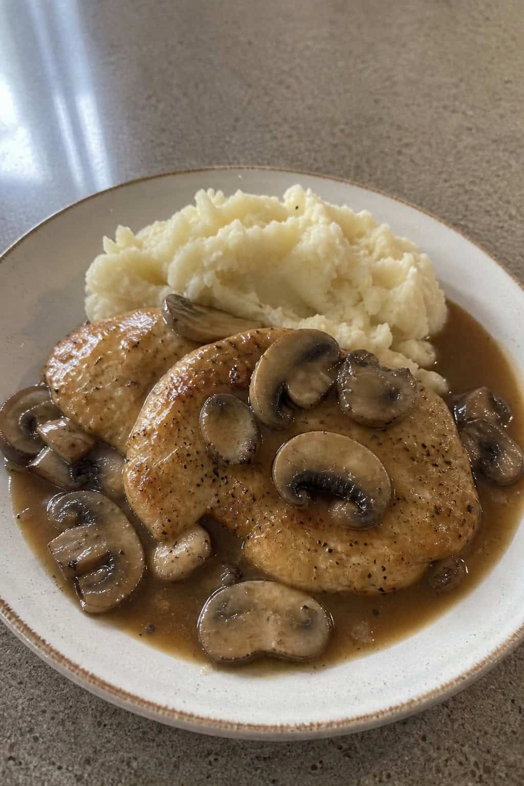 A plate of Chicken Marsala with mushrooms garnished with parsley, served with a side of mashed potatoes on a wooden table.
