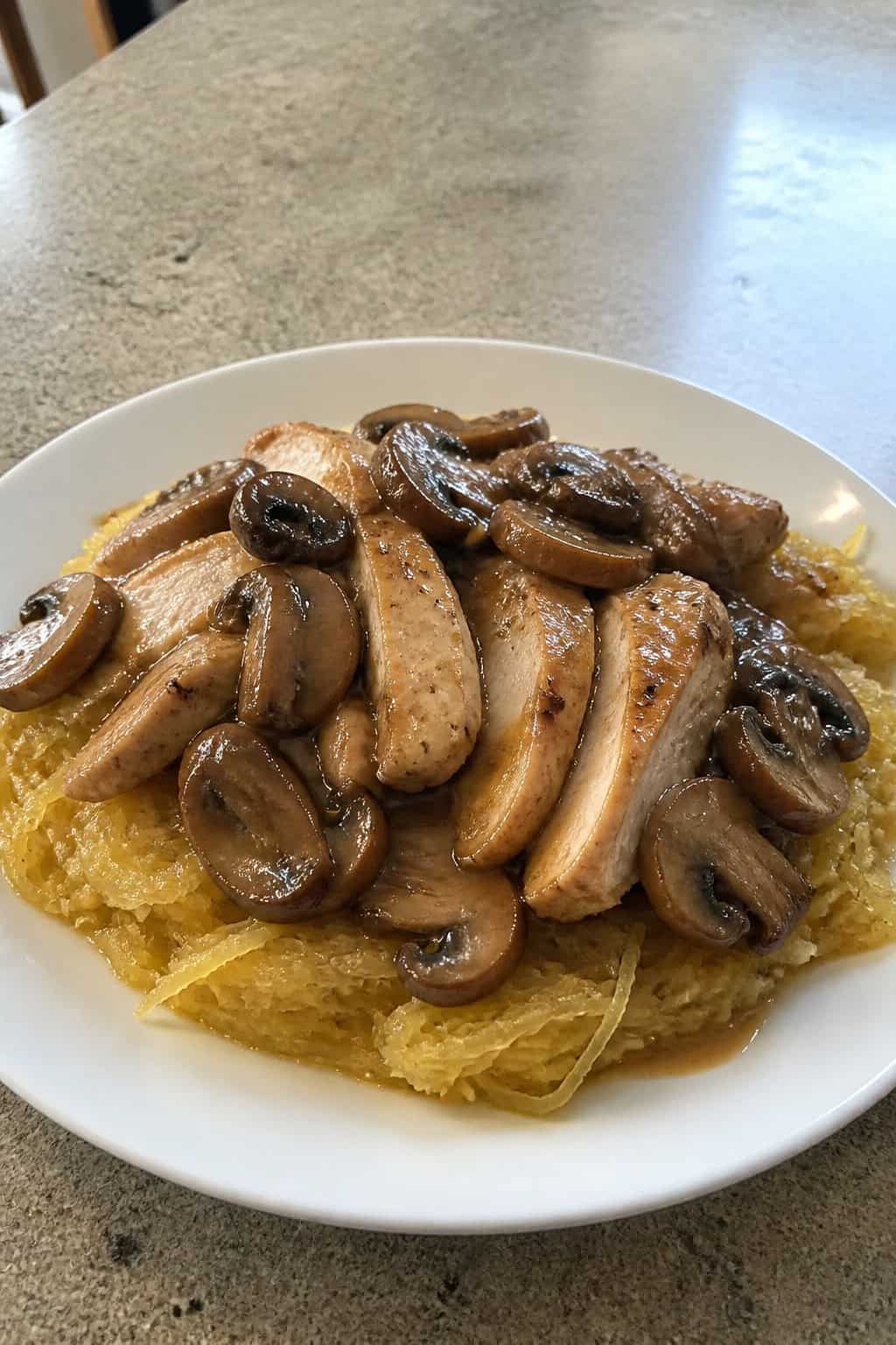 A plate of sliced chicken breast with mushroom Marsala sauce served over spaghetti squash, garnished with parsley.