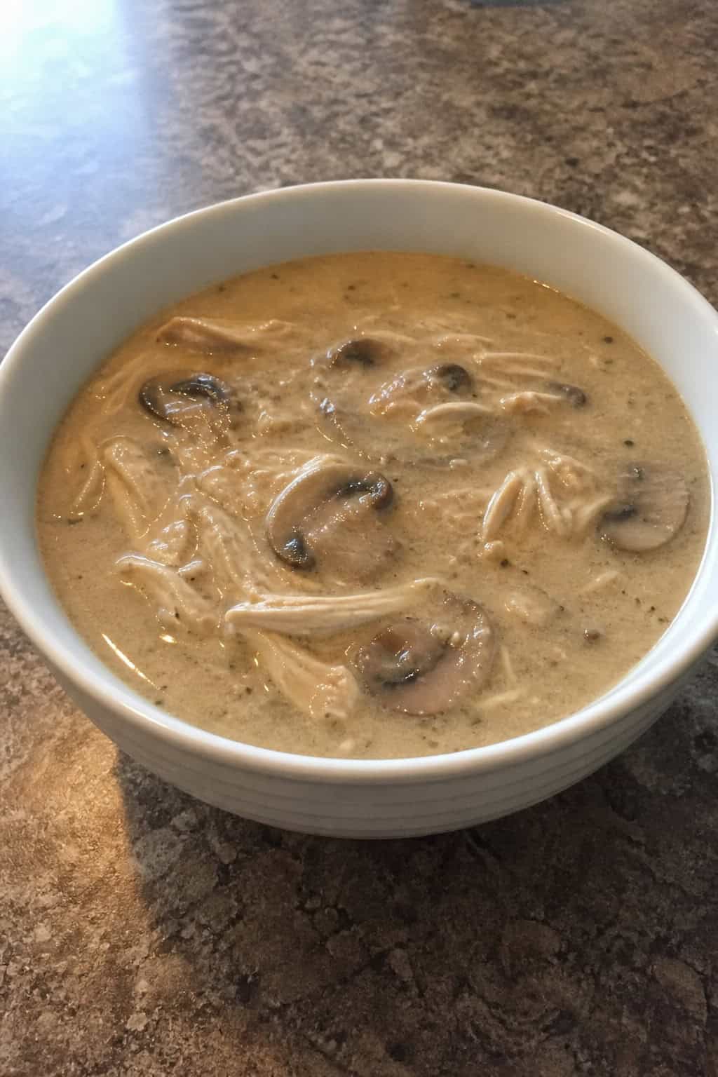 A bowl of chicken, mushroom, and thyme soup on a wooden table with fresh mushrooms and thyme nearby.