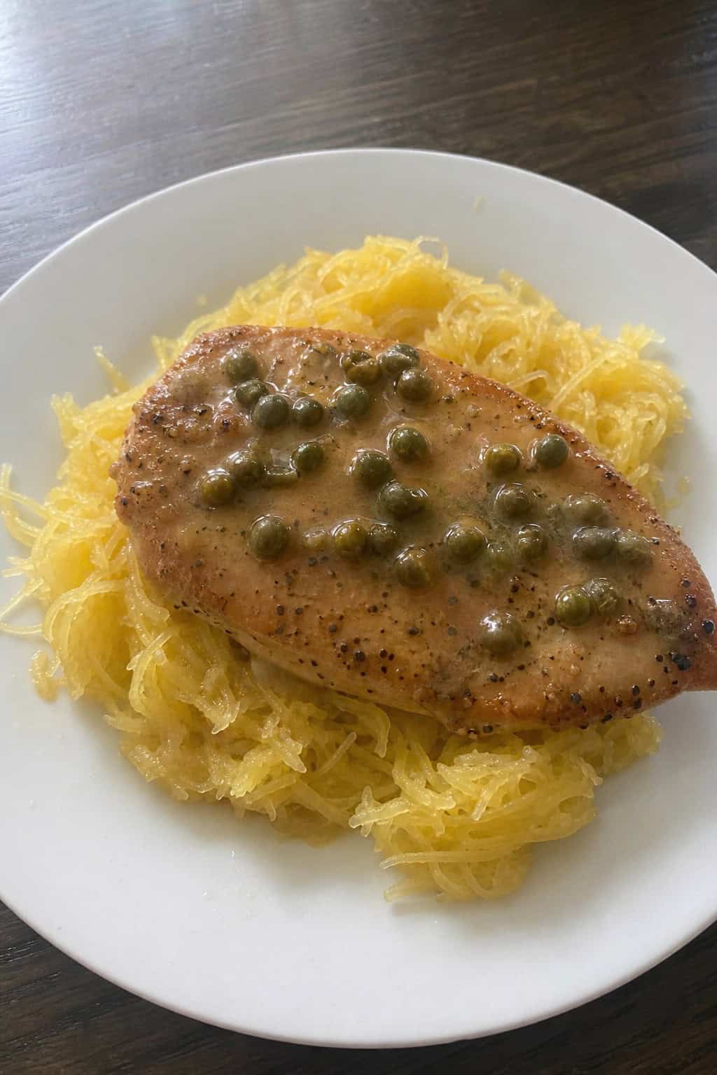 A plate of chicken piccata served over spaghetti squash with lemon sauce and parsley garnish.