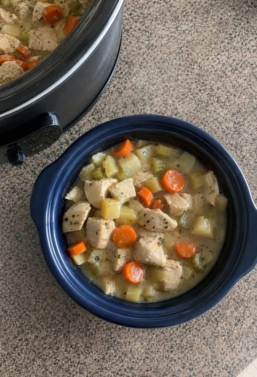 A bubbling crockpot filled with savory chicken pot pie filling, surrounded by fresh vegetables and herbs