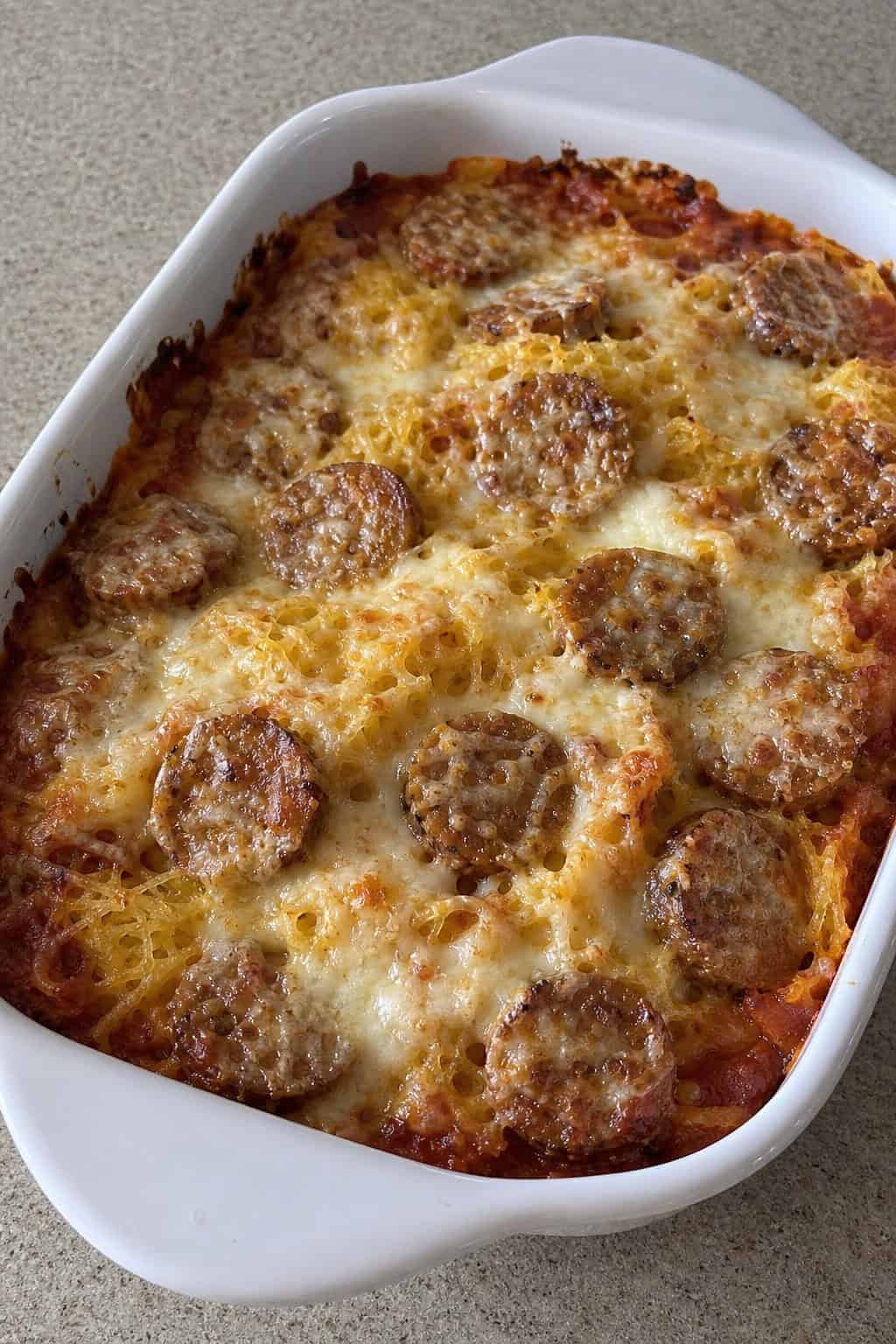 22 Chicken and Spaghetti Squash Recipes You’ll Love to Try Tonight! 16 A baked casserole dish filled with chicken sausage, spaghetti squash, melted cheese, and fresh basil on a wooden table.