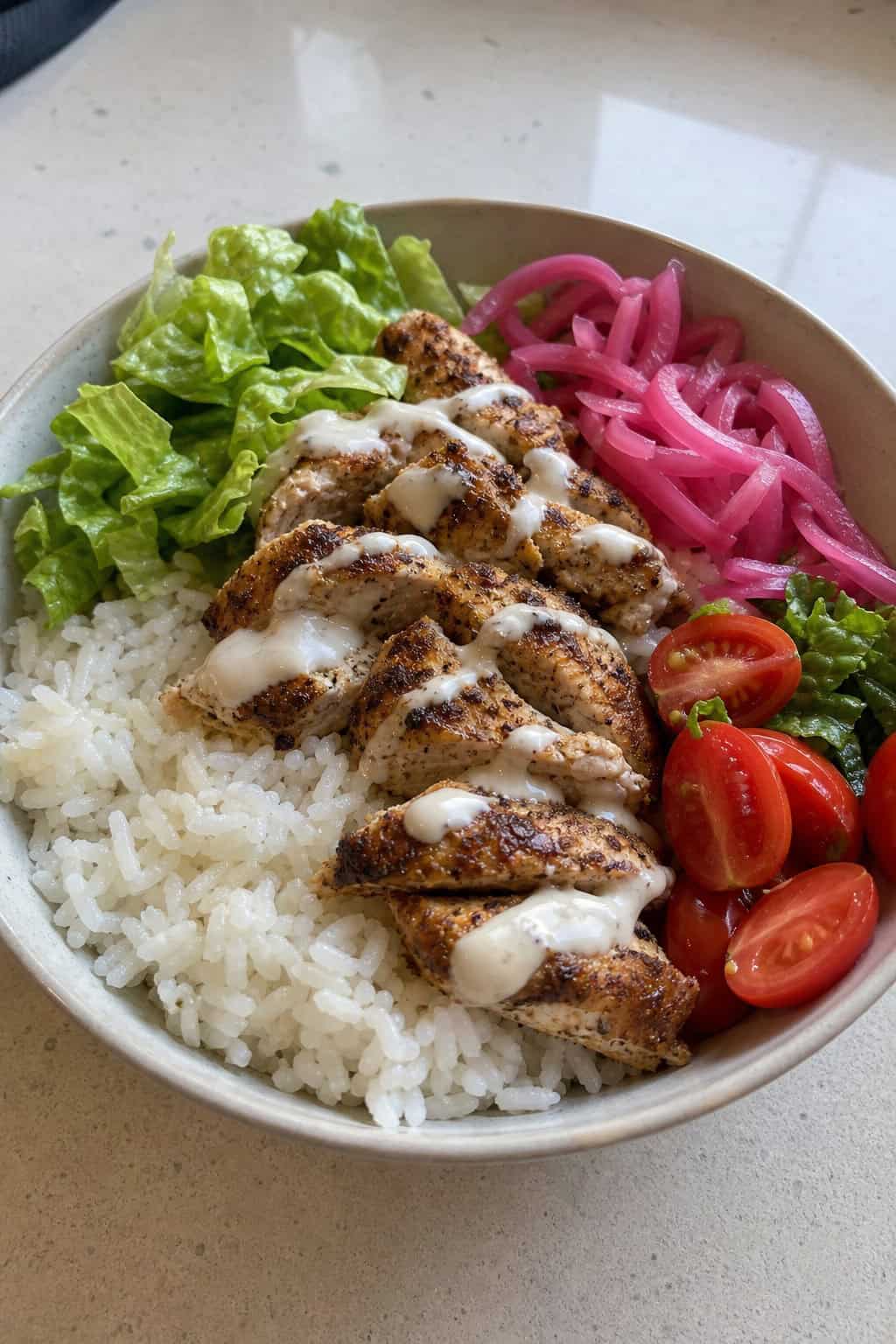 A bowl of chicken shawarma with grilled chicken breast, pickled onions, rice, greens, and cherry tomatoes.
