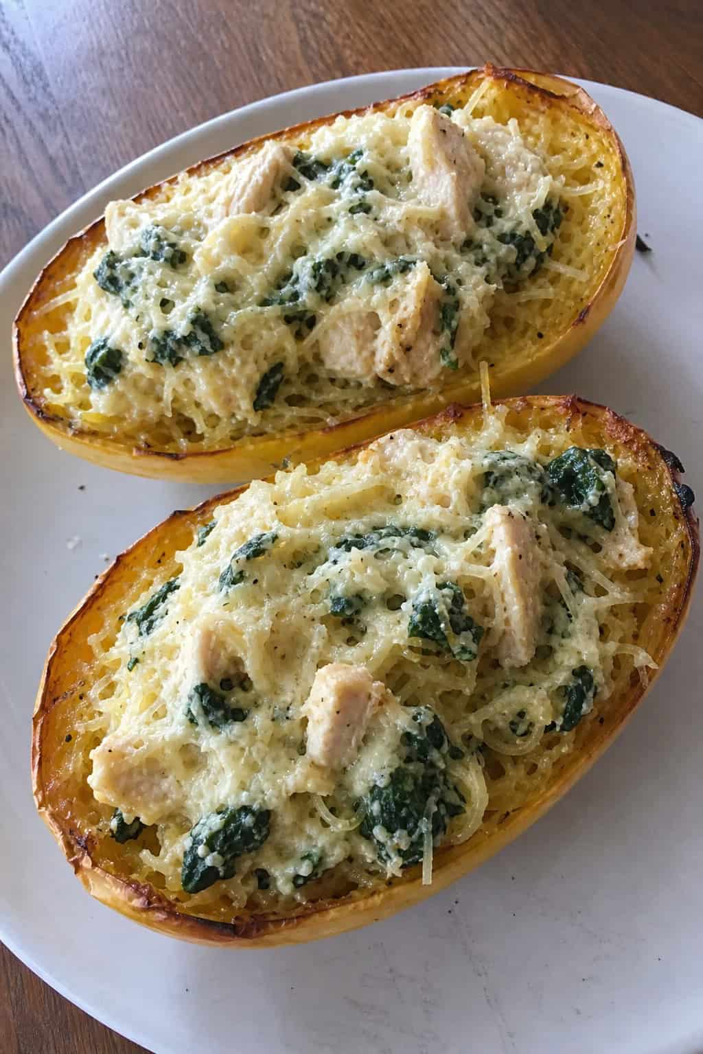 A plate of roasted spaghetti squash halves stuffed with chicken, spinach, and ricotta cheese, garnished with fresh herbs on a wooden table.